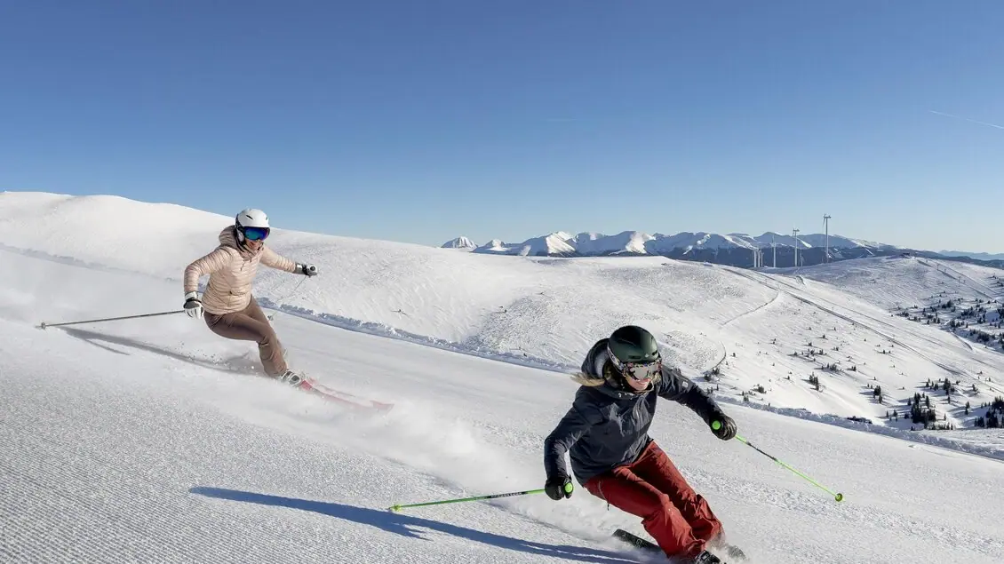 Twee skiërs op een pas geprepareerde piste in het skigebied Lachtal, met besneeuwde bergtoppen op de achtergrond