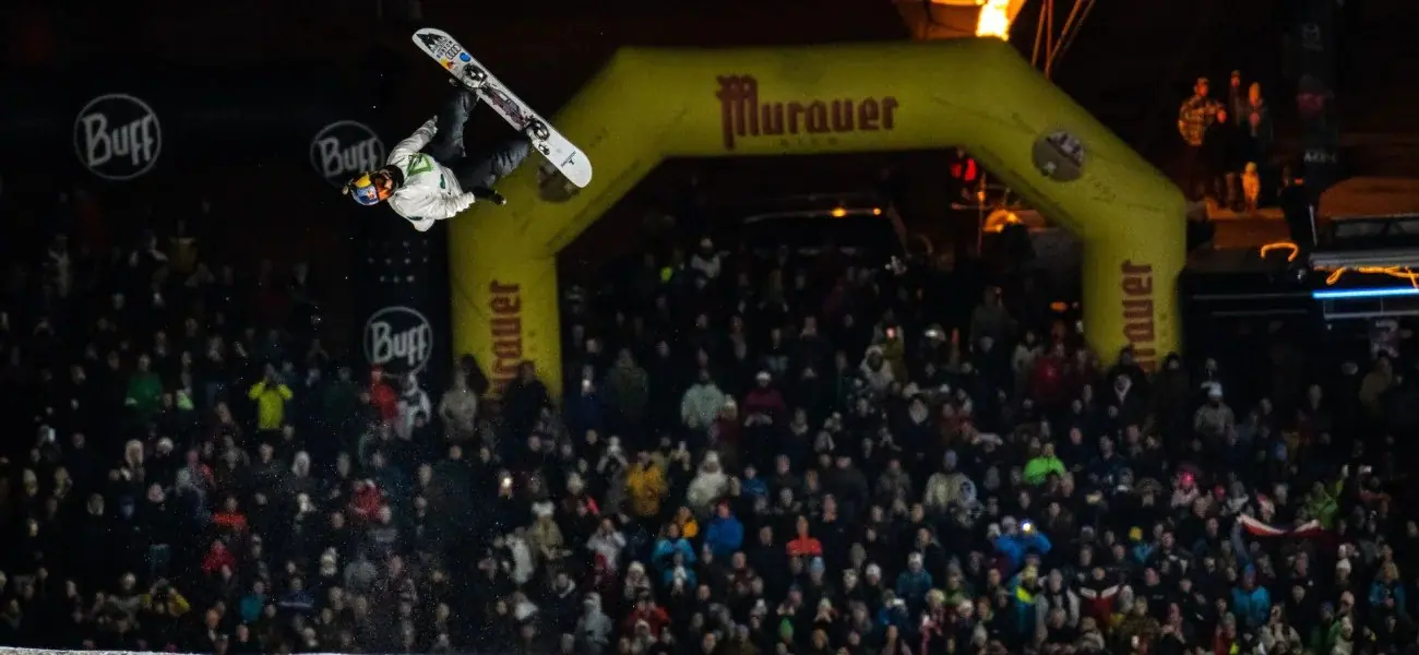 Snowboarder maakt een sprong boven een groot publiek tijdens een avondevenement aan de Kreischberg